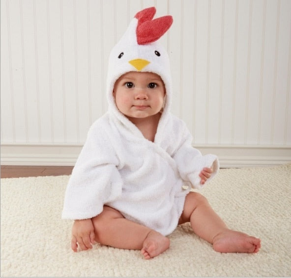 Baby iført hvid badekåbe med kyllingehætte sidder på tæppe. Sødt babybillede, kyllingekostume, børnemode, nuttet baby.