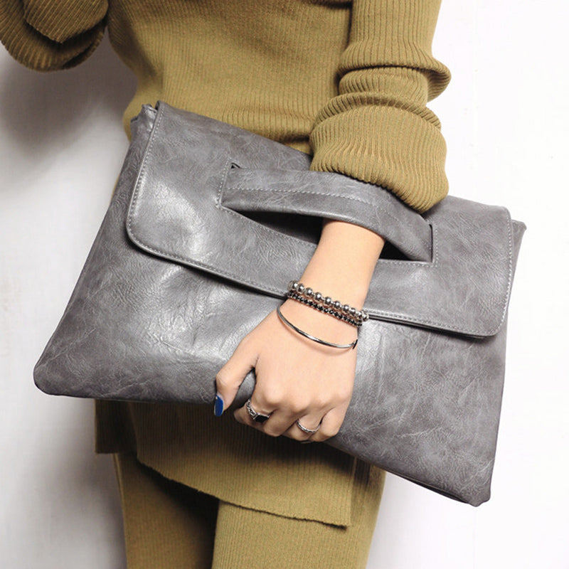 Kvinde med grå læder clutch taske, iført olivengrøn sweater. Elegant modeaccessory, perfekt til stilfulde outfits og moderne look.