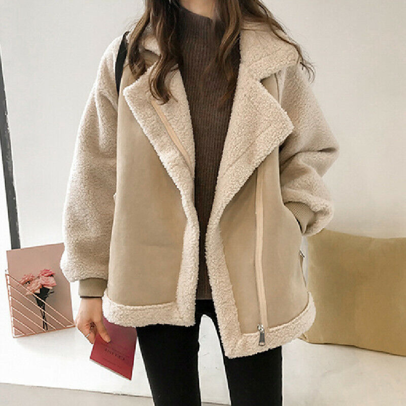 Kvinde iført beige teddyjakke og brun sweater, holder en lyserød bog. Mode, vinterjakke, trendy overtøj, casual stil.