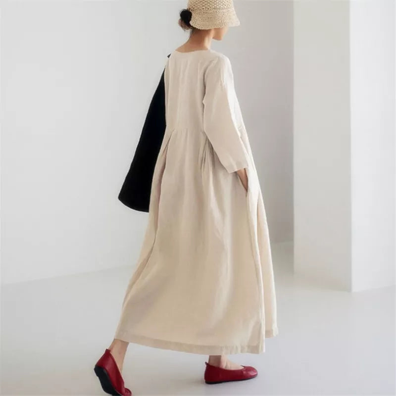 Kvinde i lang, beige kjole og røde sko, bærer sort taske og stråhat. Minimalistisk mode, elegant stil, moderne kvindetøj, skandinavisk design.