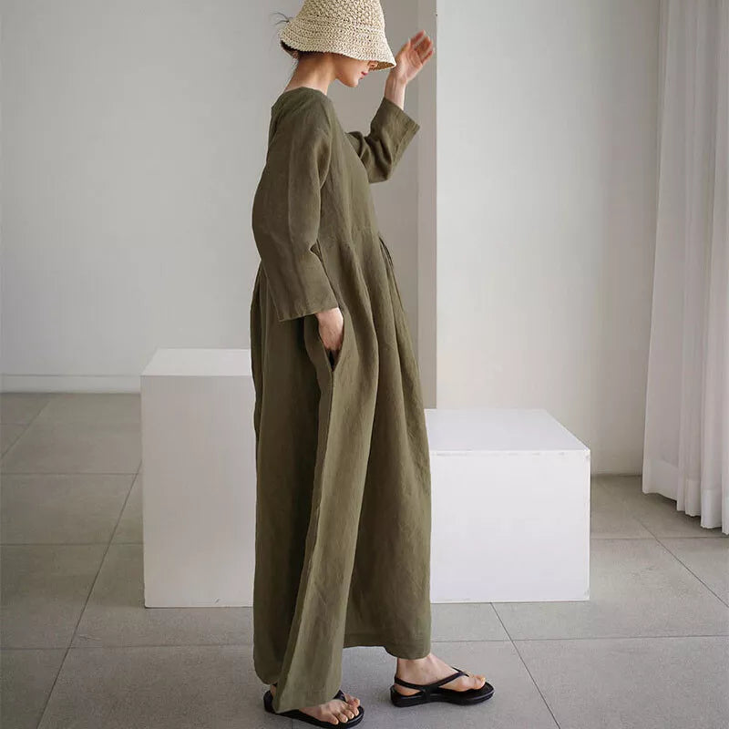Kvinde i lang, olivengrøn kjole og stråhat står i minimalistisk rum. Mode, sommerkjole, skandinavisk stil, afslappet elegance, moderne design.