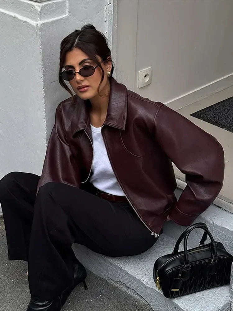 Kvinde i brun læderjakke og solbriller sidder på trappe med sort taske ved siden af. Mode, street style, trendy outfit, moderne kvindetøj.