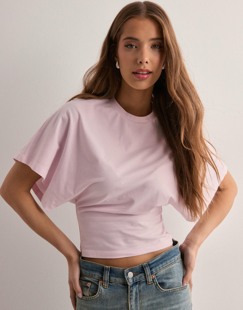 Ung kvinde i lyserød T-shirt og jeans foran hvid baggrund. Mode, casual stil, langhåret, moderne tøj.