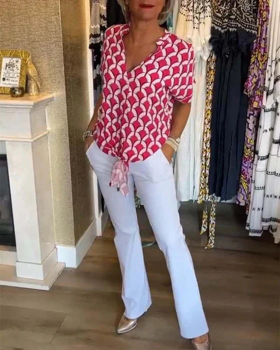 Kvinde iført pink mønstret bluse og hvide bukser i tøjbutik. Mode, stilfuldt outfit, moderne kvindetøj, shopping.
