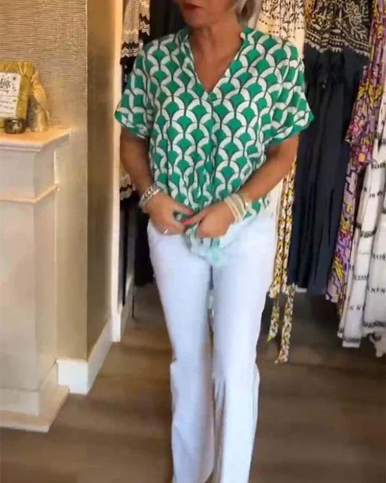 Kvinde iført grøn mønstret bluse og hvide bukser i tøjbutik. Moderne damemode, stilfuldt outfit, shopping, trendy beklædning.