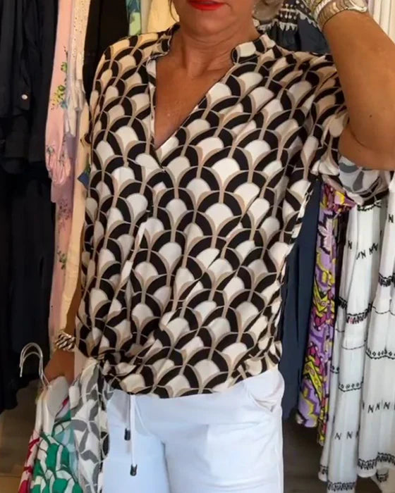Dame i mønstret bluse med geometrisk design og hvide bukser i tøjbutik. Moderne mode, stilfuldt outfit, shopping.