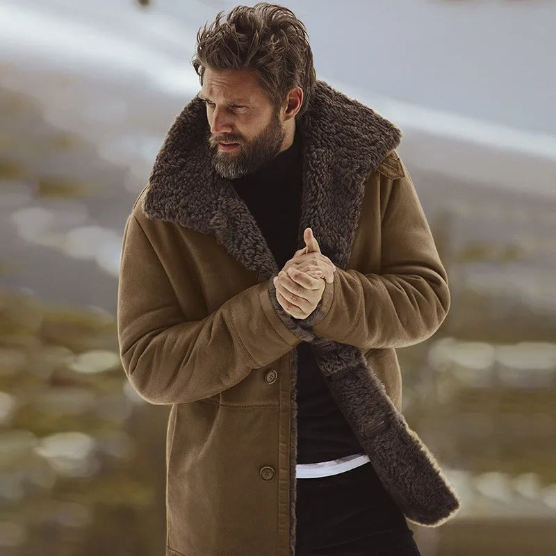 Mand iført brun fåreskindfrakke med pelskrave, står udendørs i vinterlandskab. Varm vintermode, stilfuld herrejakke, elegant overtøj.
