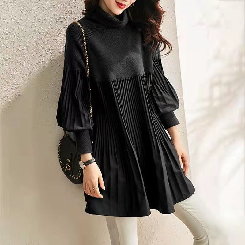 Kvinde iført sort plisseret kjole med lange ærmer og høj hals, poserer mod en lys væg. Elegant mode, moderne design, stilfuldt outfit.