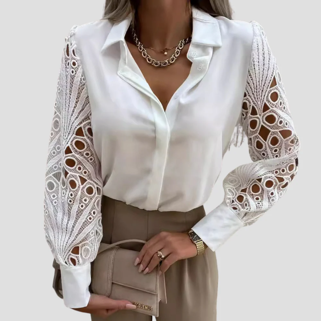 Elegant kvinde i hvid bluse med blondeærmer, beige bukser og guldhalskæde, holder en lille beige taske. Mode, stilfuldt outfit, moderne kvindetøj.