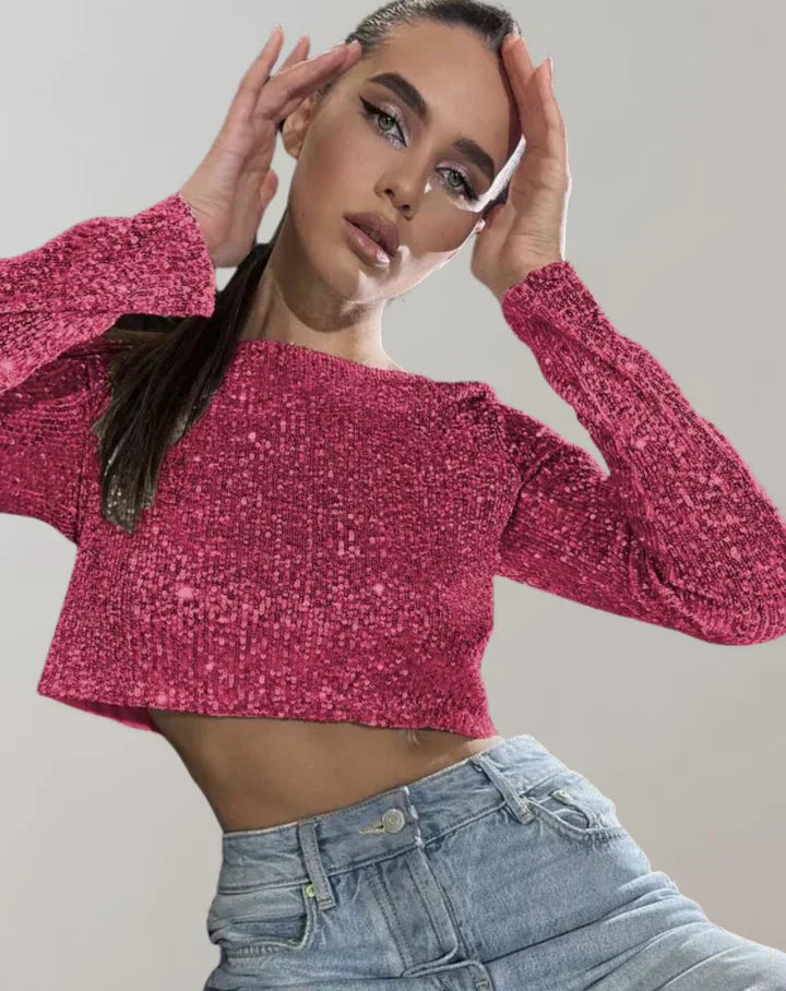 Kvinde i pink glitrende trøje og blå jeans, poserer med hænderne ved ansigtet. Moderne mode, stilfuldt outfit, trendy tøj.