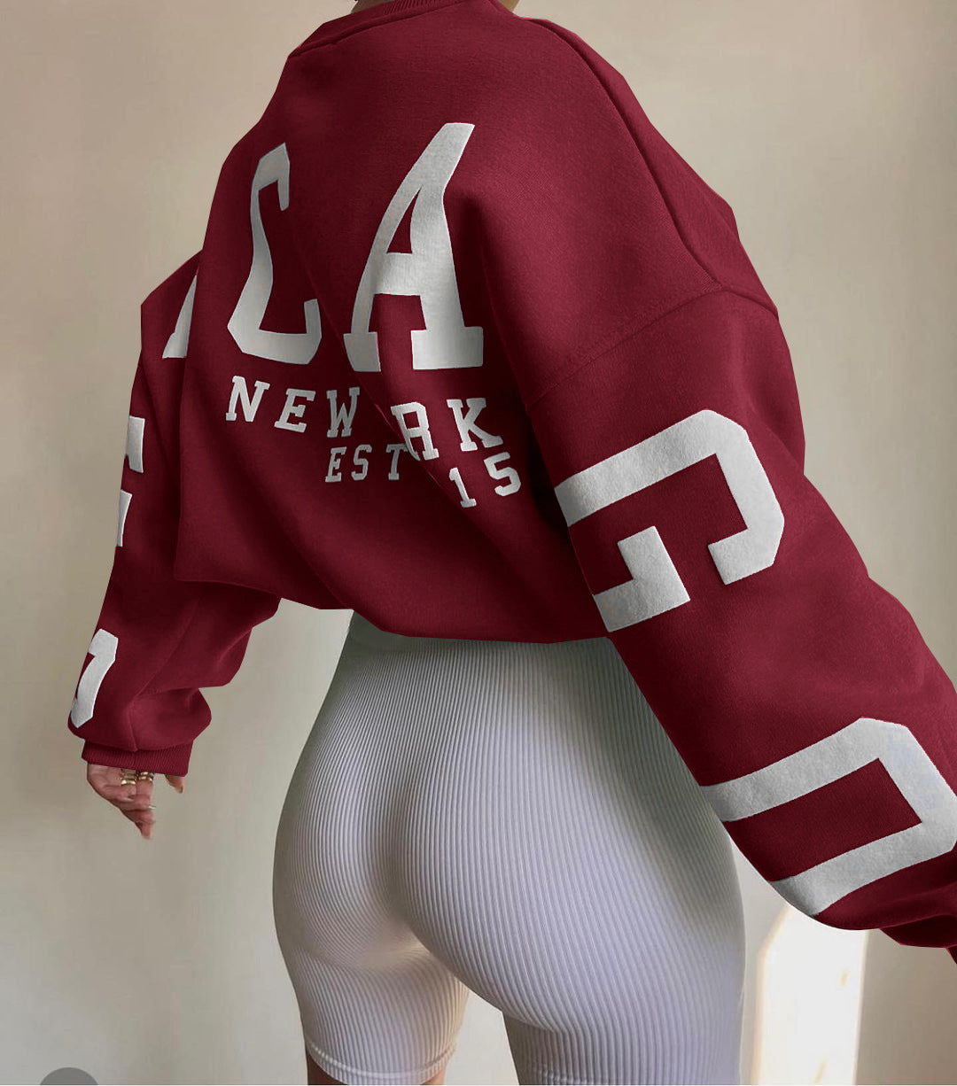 Rød sweatshirt med hvid tekst "NEW YORK EST 15" og hvide cykelshorts. Mode, streetwear, afslappet stil, trendy tøj, moderne design.