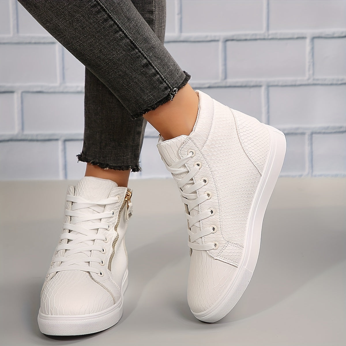 Hvide højtop sneakers med krokodillemønster og lynlåsdetalje, bæres af person i grå jeans. Moderne fodtøj til kvinder, stilfuldt og komfortabelt.