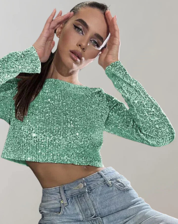 Kvinde i grøn glitrende top og blå jeans, poserer med hænderne ved ansigtet. Moderne mode, glamourøst look, trendy tøjstil.