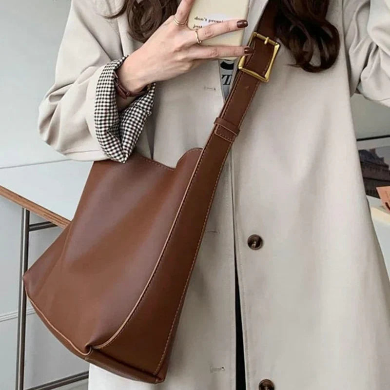 Brun læder skuldertaske bæres af kvinde i beige frakke. Stilfuldt tilbehør, mode, hverdagsbrug, trendy design, praktisk taske.
