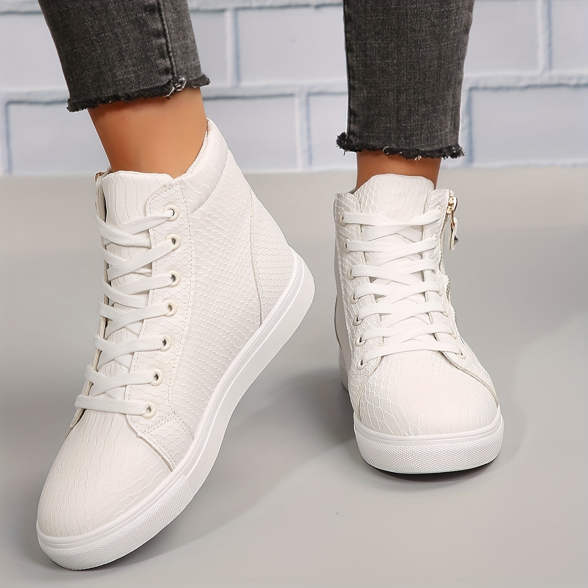 Hvide højtop sneakers med snørebånd og lynlås, krokodillemønster, bæres af person i grå jeans. Moderne fodtøj til kvinder, stilfuldt og komfortabelt.