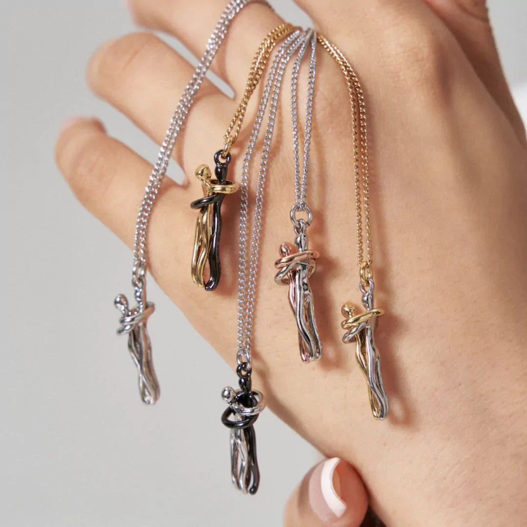 Hånd med fem kæder i sølv og guld, hver med unikke, abstrakte vedhæng. Moderne smykker, elegant design, stilfulde halskæder.