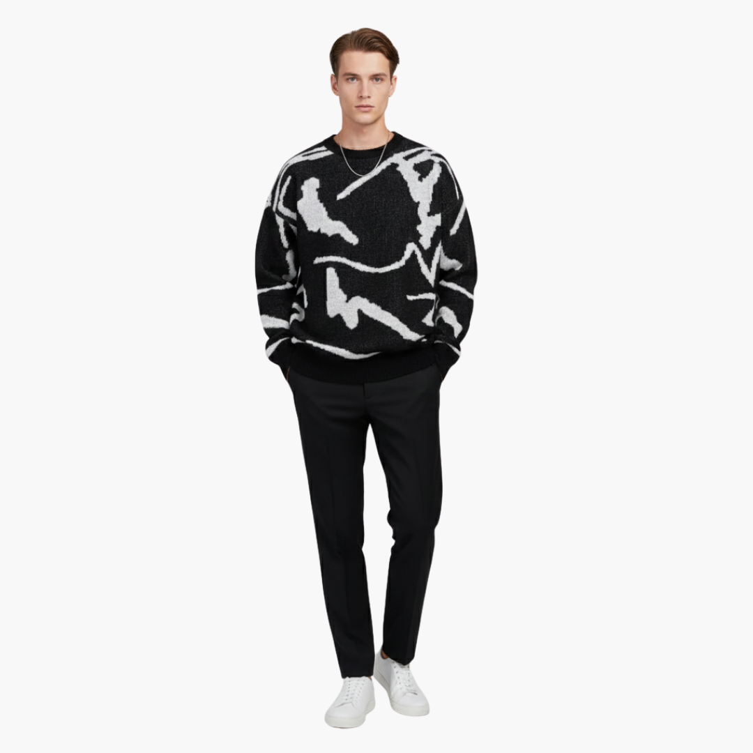 Mand iført sort-hvid mønstret sweater, sorte bukser og hvide sneakers. Moderne herremode, afslappet stil, minimalistisk design.