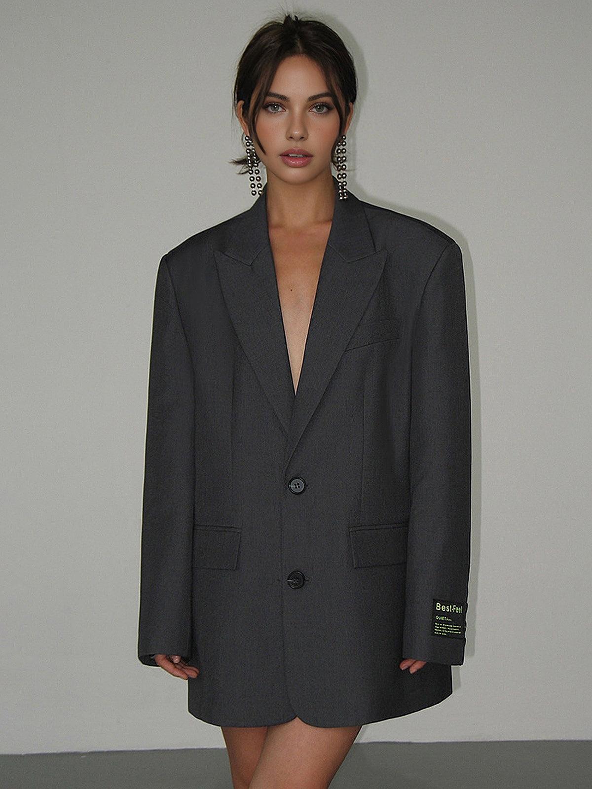 Kvinde iført oversize grå blazer, minimalistisk mode, trendy look, store øreringe, moderne stil, elegant tøj, fashionabelt outfit.