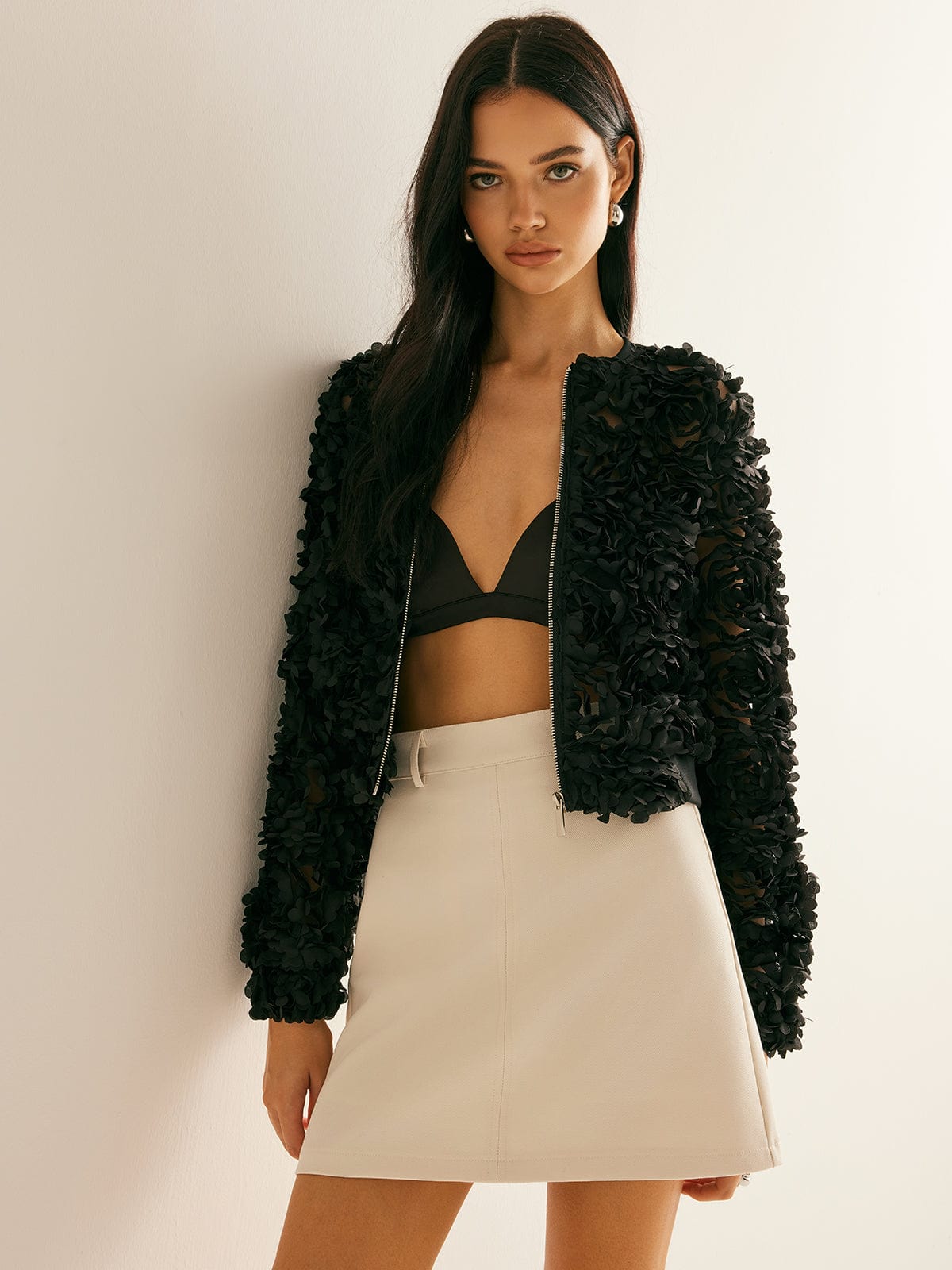 Ung kvinde iført sort blomstret jakke, sort top og beige nederdel. Mode, stilfuldt tøj, moderne kvindemode, elegant outfit.