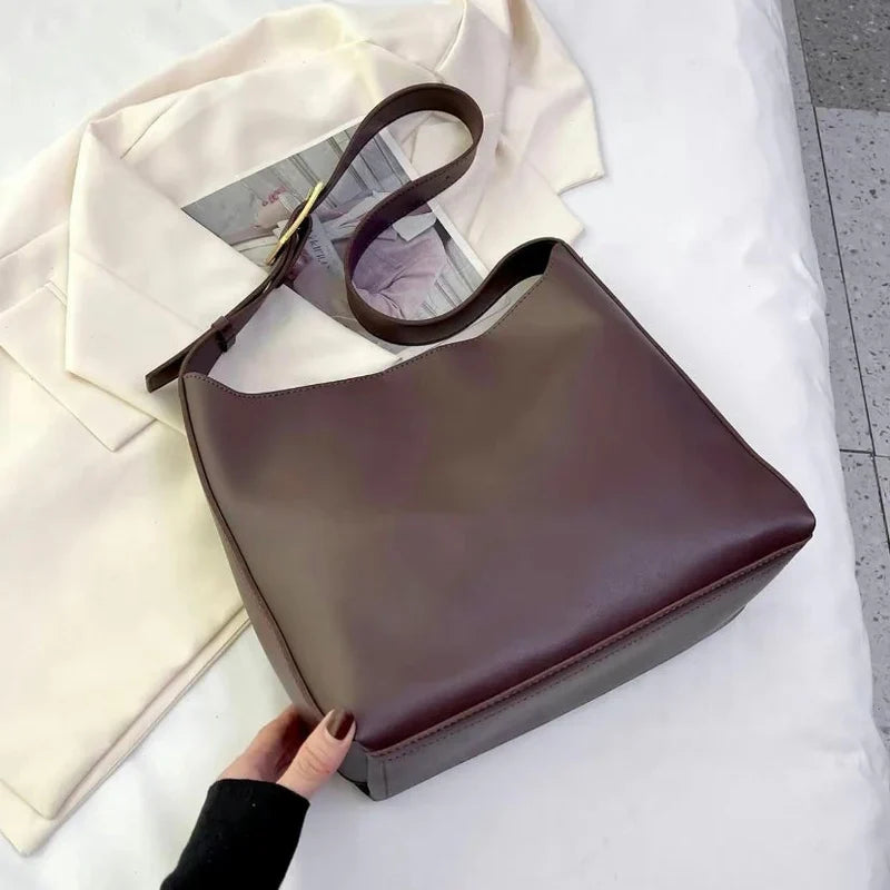 Brun læderhåndtaske på hvid jakke, minimalistisk design, kvindemode, stilfuldt tilbehør, moderne skuldertaske, elegant og praktisk.