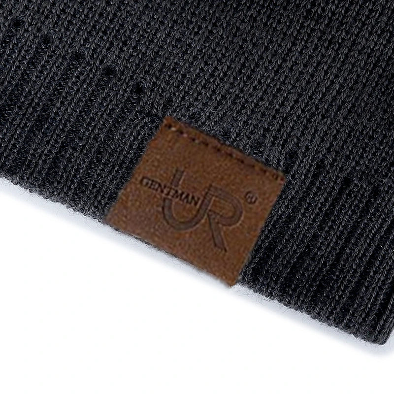 Sort strikket hue med brun lædermærke, der viser "UR" logo. Stilfuldt vintertilbehør, perfekt til kolde dage. Unisex design, moderne og praktisk.