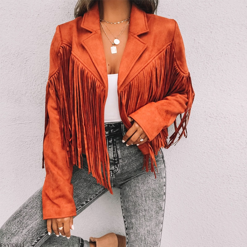 Kvinde iført orange ruskindsjakke med frynser, hvid top og grå jeans. Trendy boho-stil, perfekt til efterårsmode.