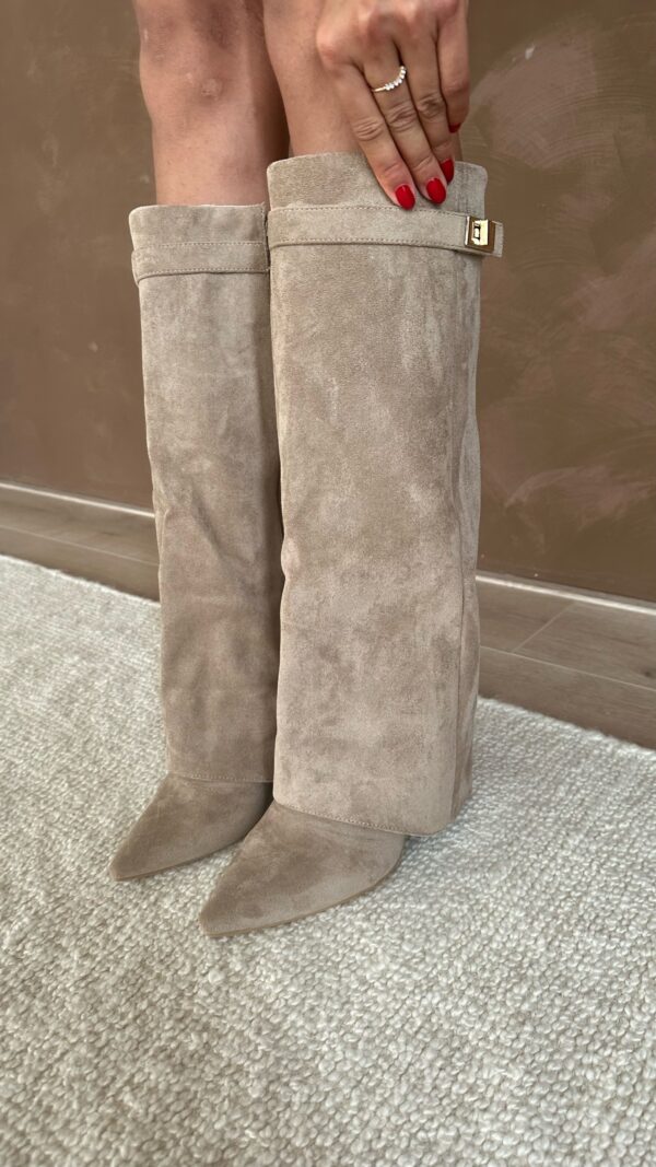 Beige ruskindsstøvler med spids tå og spænde, bæres af person på tæppe. Perfekte til efterårsmode og stilfulde outfits.