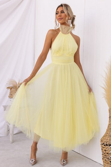 Kvinde i gul tylkjole med halterneck, poserer elegant. Perfekt til bryllup eller fest. Moderne mode, stilfuldt design, sommerkjole.