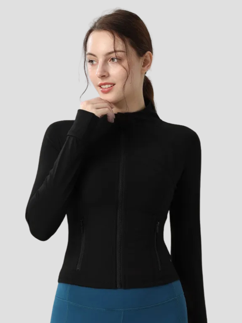 Kvinde iført sort træningsjakke med lynlås og blå leggings, ser til siden. Sportstøj, fitnessmode, aktiv livsstil.