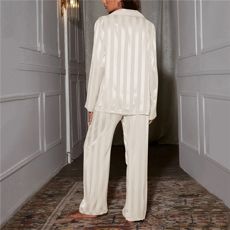 Kvinde iført hvidt, stribet satin pyjamasæt i elegant gang. Komfortabelt nattøj, luksuriøst design, perfekt til afslapning og søvn.