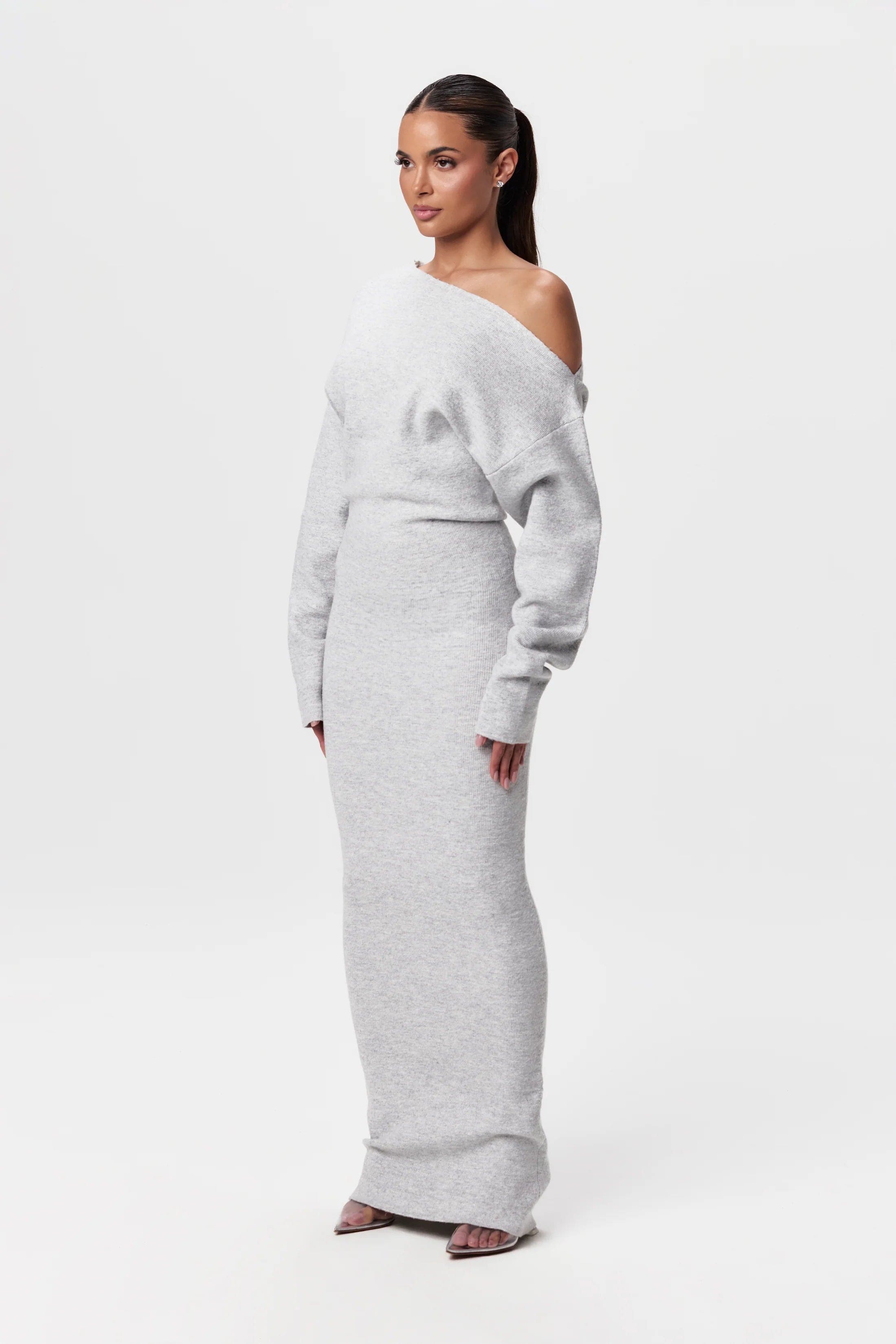 Kvinde iført lang, grå off-shoulder kjole, elegant og minimalistisk design, perfekt til modebevidste kvinder. Ideel til festlige lejligheder.