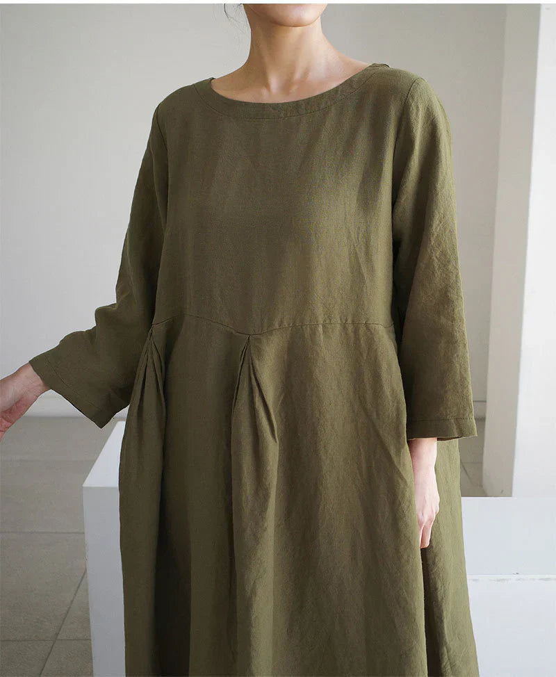 Kvinde iført en løs, olivengrøn kjole med lange ærmer og rund halsudskæring. Minimalistisk design, komfortabelt hverdagslook.