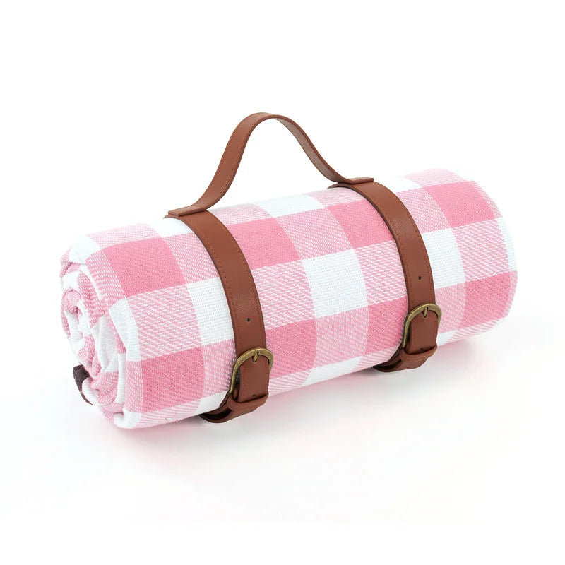 Lyserødt og hvidt ternet picnic-tæppe med brunt læderhåndtag og stropper, perfekt til udendørs brug og picnic i parken.