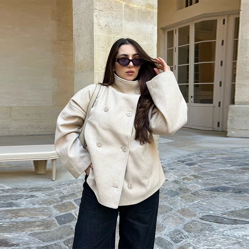 Kvinde i beige frakke og solbriller står på brostensbelagt gårdsplads. Mode, efterårstøj, stilfuldt look, udendørs.