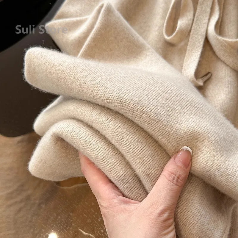 Hånd holder blød beige cashmere sweater, tæt tekstur, luksuriøst strik, vintermode, komfortabelt tøj, elegant design, varm beklædning.