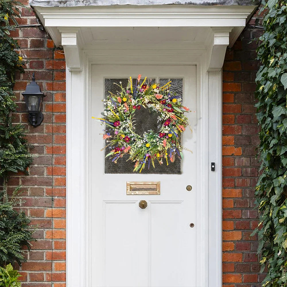 Hvid dør med farverig blomsterkrans, murstensvæg og grønne planter. Perfekt til forårsdekoration og indgangspynt.