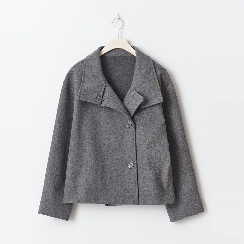 Grå uldjakke til kvinder med brede revers og knaplukning, hængende på bøjle. Stilfuld og moderne design, perfekt til efterår og vinter.