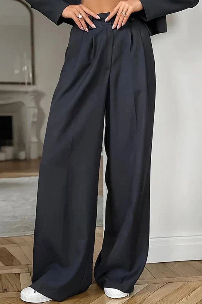 Kvinde iført sorte, løstsiddende bukser med høj talje og vide ben, kombineret med hvide sneakers. Moderne mode, komfortabelt tøj, stilfuldt look.