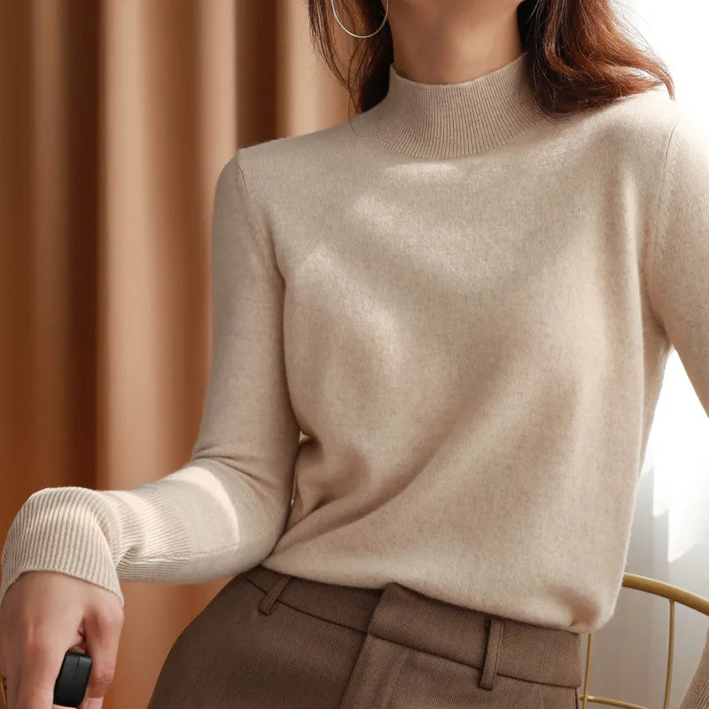 Kvinde iført beige rullekrave sweater og brune bukser, sidder på en stol. Elegant efterårsoutfit, minimalistisk mode, stilfuldt tøjvalg.