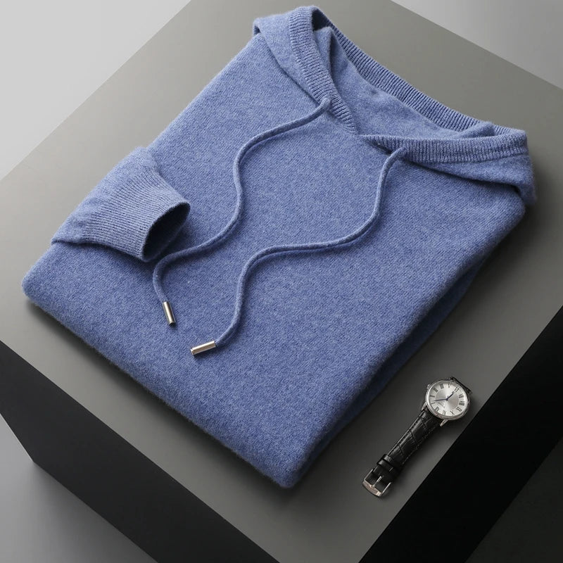 Blå cashmere hættetrøje foldet på grå overflade ved siden af elegant sort læderrem ur. Luksuriøs striktrøje, stilfuldt herreur.