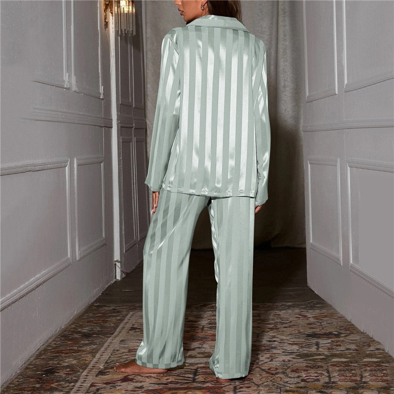 Kvinde iført lysegrønt, stribet satin pyjamasæt i elegant gang. Komfortabelt nattøj, moderne design, luksuriøs stil, perfekt til afslapning.
