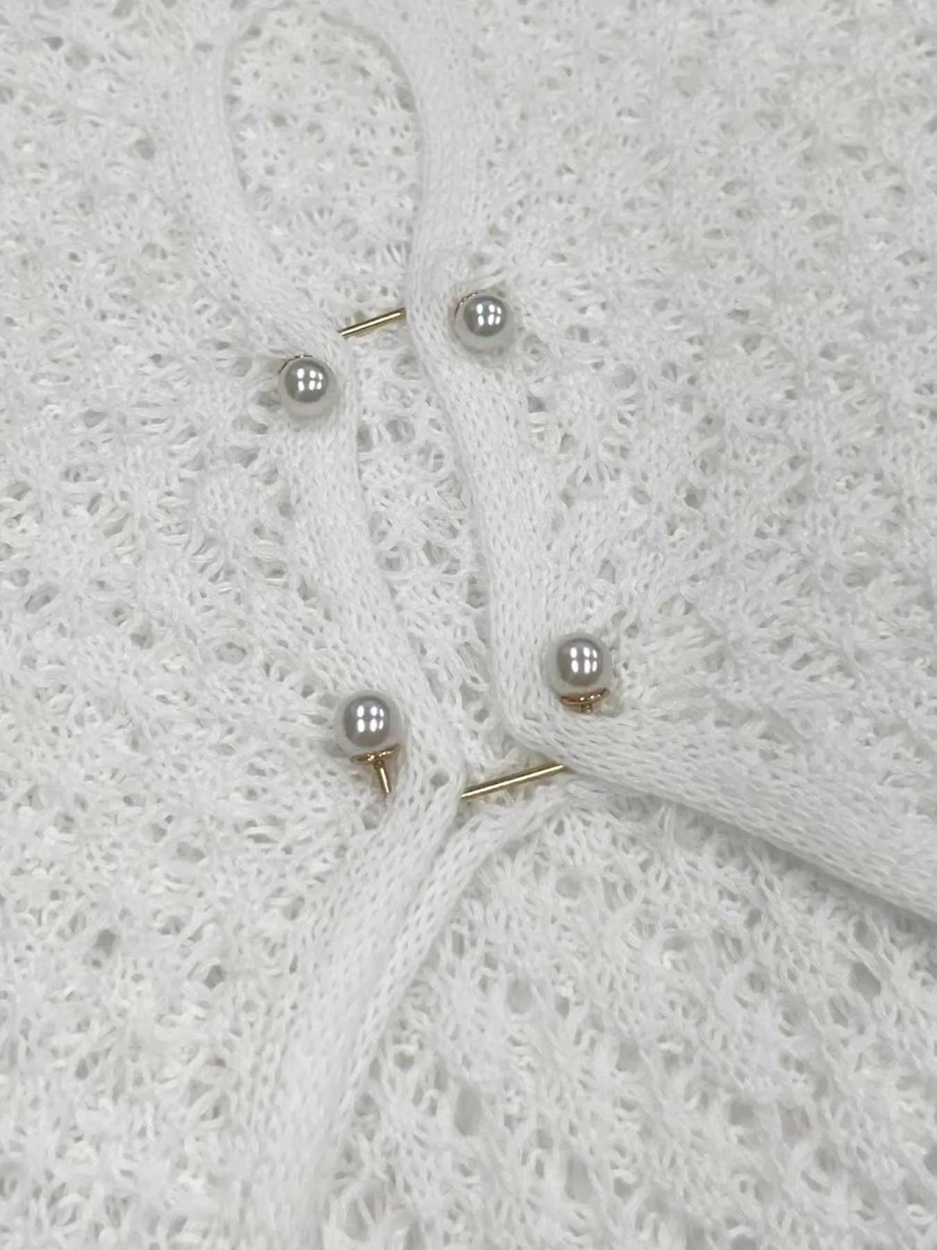 Hvid strikket cardigan med perleknapper og delikat hulmønster. Elegant design, perfekt til modebevidste kvinder. Luksuriøst og stilfuldt tøjvalg.