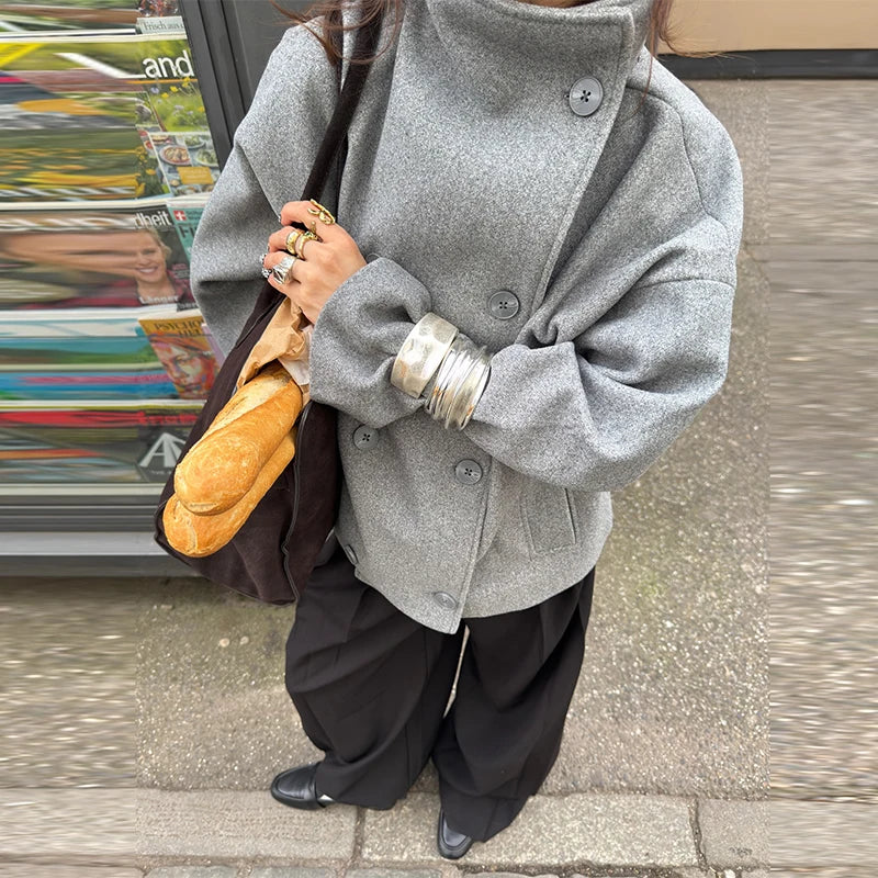 Kvinde i grå frakke med brød i taske, iført sorte bukser og sølvsmykker. Gadebillede, mode, efterårstøj, casual stil.