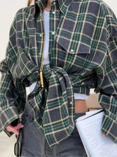 Kvinde iført grønternet skjorte bundet foran, grå jeans og hvid top. Holder dokumenter. Trendy afslappet mode, efterårslook, street style.