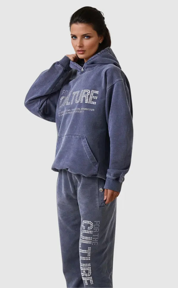 Kvinde iført blå hættetrøje og joggingbukser med "CULTURE" tryk, afslappet mode, komfortabelt tøj, moderne streetwear stil.
