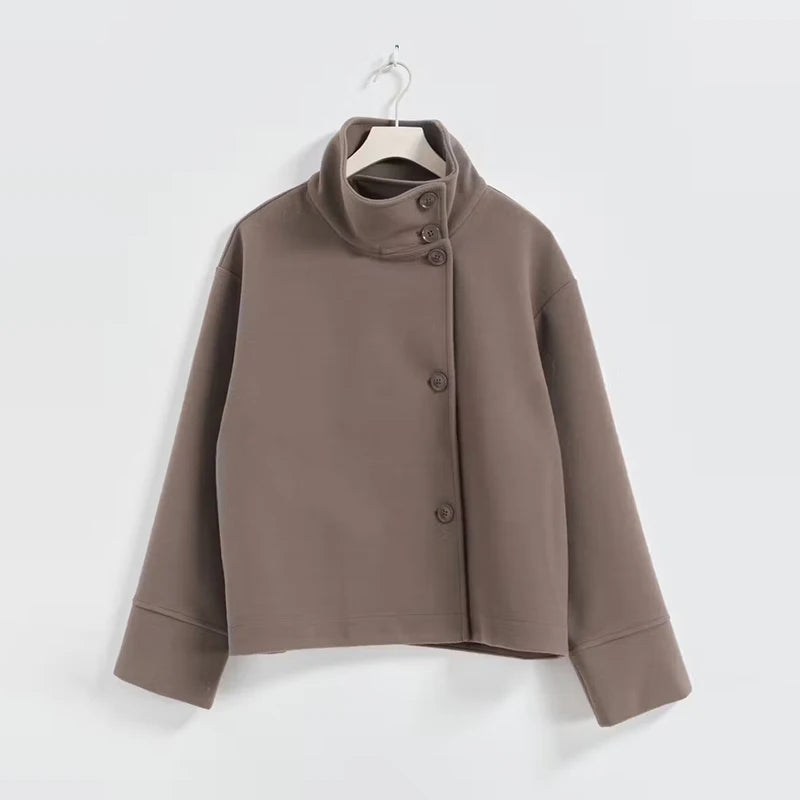 Brun jakke med asymmetrisk knaplukning og høj krave, hængende på bøjle. Moderne design, minimalistisk stil, perfekt til efterårsmode.