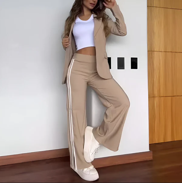 Kvinde iført beige jakkesæt med hvide striber og hvid top, poserer mod hvid væg. Moderne mode, afslappet stil, trendy outfit.