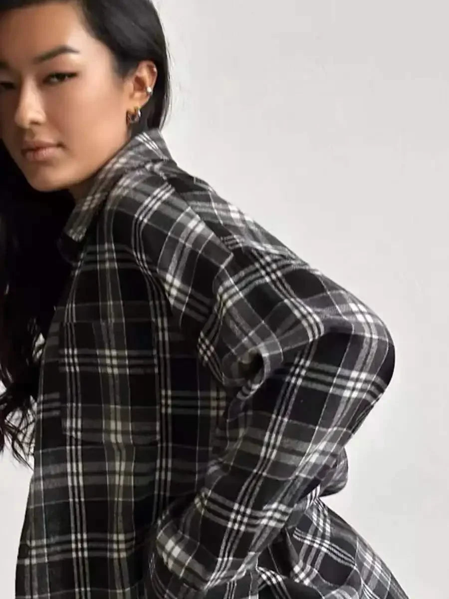 Kvinde iført sort-hvid ternet skjorte, poserer mod en neutral baggrund. Trendy mode, afslappet stil, moderne kvindetøj, plaid skjorte.