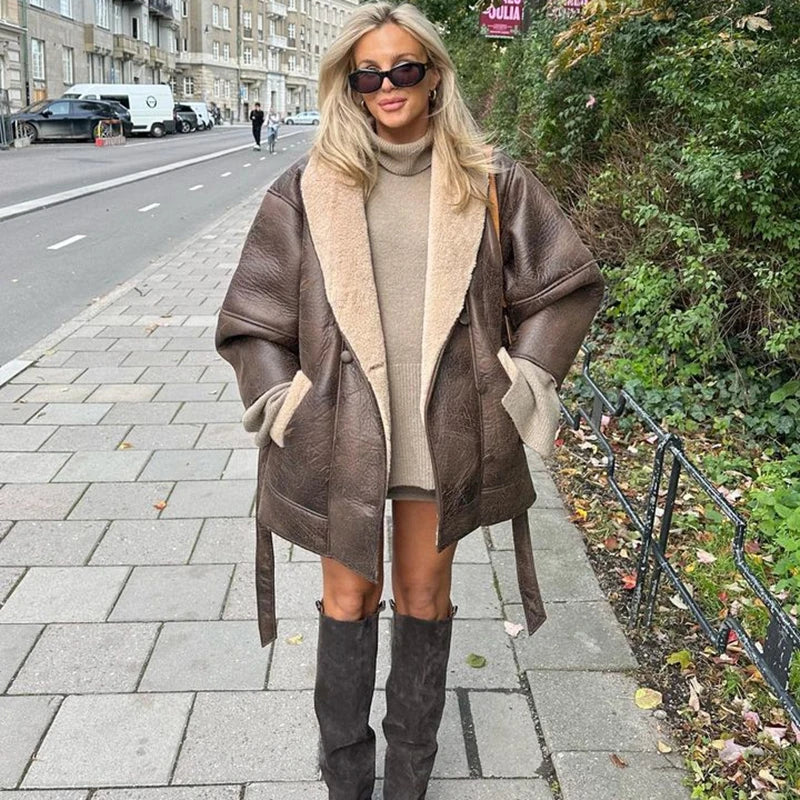 Kvinde iført brun læderjakke og knæhøje støvler på fortov i bymiljø. Mode, efterårstøj, stilfuldt look, gadebillede, urban stil.