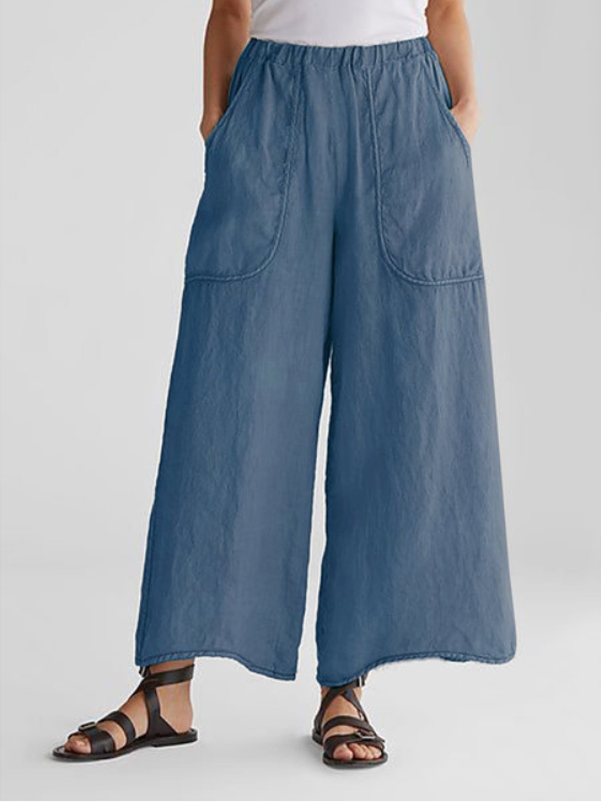 Person iført blå, løstsiddende bukser med store lommer og sorte sandaler. Komfortabelt og stilfuldt tøj til afslappet sommermode.